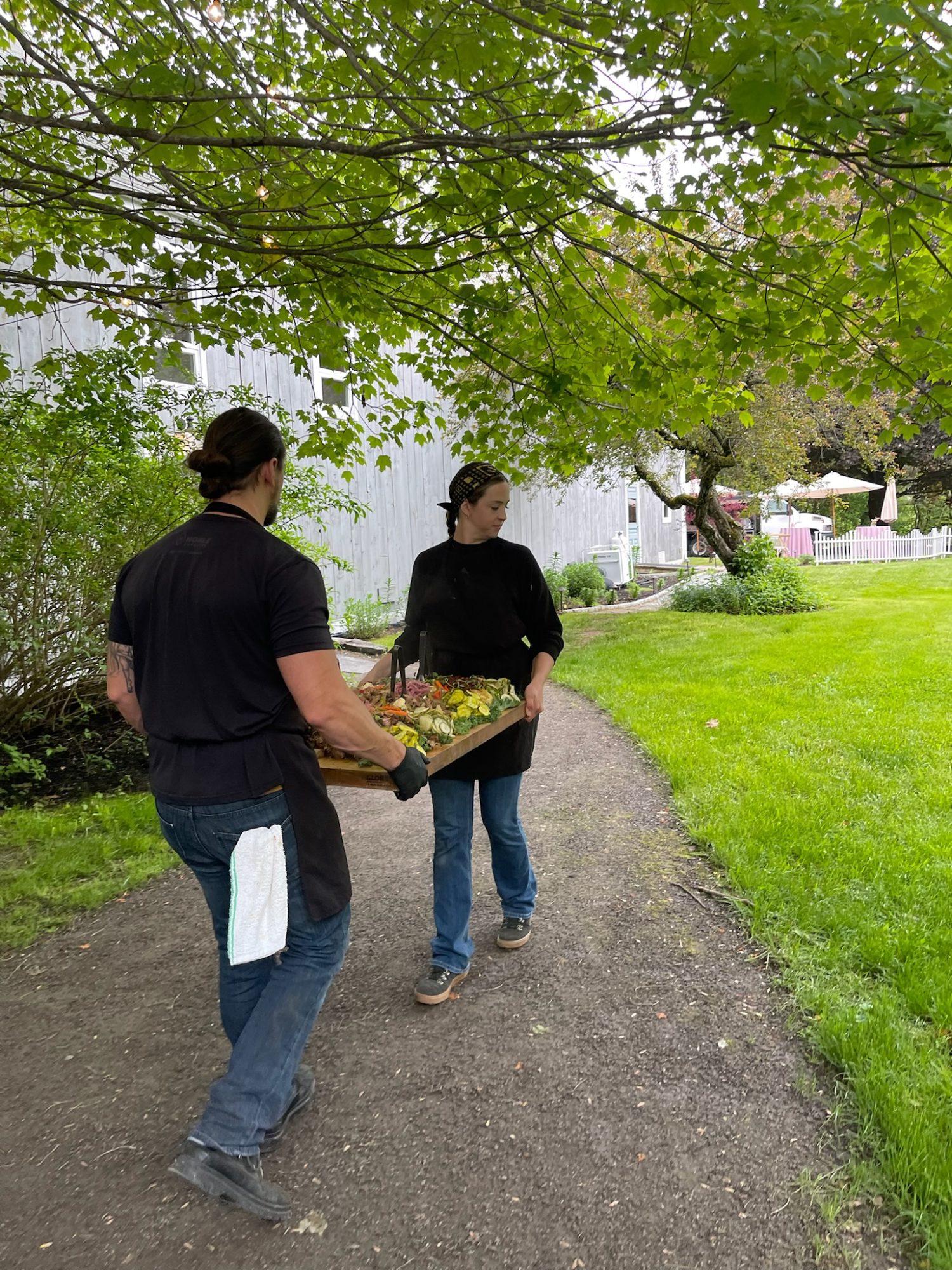 Coastline Weddings team carrying florals up a garden path during setup for a Maine wedding